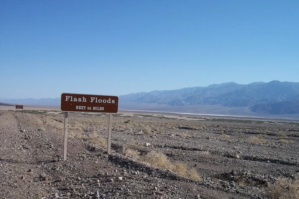 Brown and white "flash floods: next 55 miles" road sign in Death Valley, California